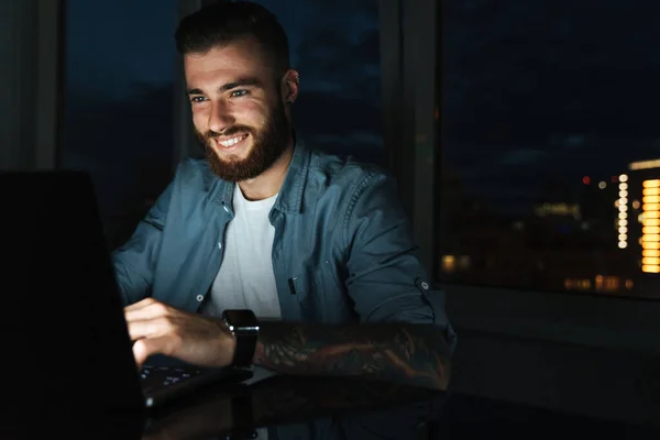 Jovem Sorridente Trabalhando Computador Portátil Enquanto Senta Mesa Dentro Casa — Fotografia de Stock