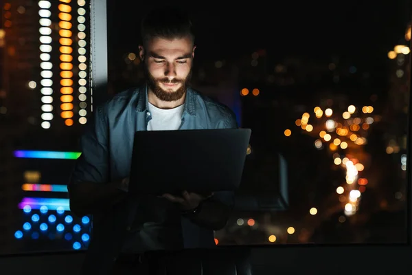 Soustředěný Mladý Muž Pracující Notebooku Když Stojí Noci Před Oknem — Stock fotografie