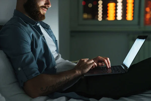 Sorrindo Jovem Barbudo Deitado Cama Casa Noite Trabalhando Computador Portátil — Fotografia de Stock