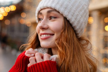 Şehir caddesinde duran, kışlık ceket ve şapka giyen neşeli, genç bir kıza yaklaş.