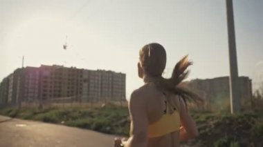 Spor kıyafetli genç bir kadının arka görüntüsü sabah dışarıda koşuyor.