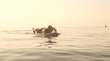 Gün batımında denizde yüzen konsantre kas sörfçüsünün yan görüntüsü