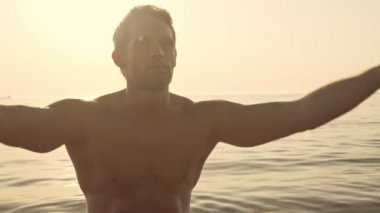 Ciddi bir kas sörfçüsü gün batımında denizde meditasyon yapıyor.