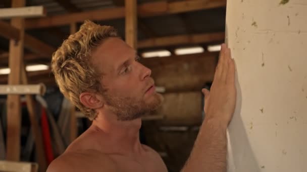 Skoncentrowany Muskularny Surfer Czyści Deskę Surfingową Zachodzie Słońca Magazynie Surfingowym — Wideo stockowe