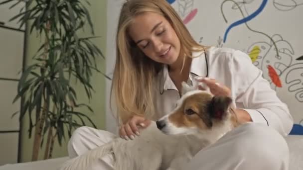 Miła Młoda Kobieta Białej Piżamie Pieści Swojego Psa Leżąc Łóżku — Wideo stockowe