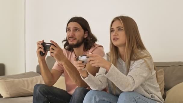 一对在沙发上快乐的年轻夫妇在家里用操纵杆玩电子游戏 — 图库视频影像