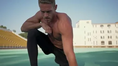 Yakışıklı genç bir sporcu stadyumda esneme hareketleri yapıyor.