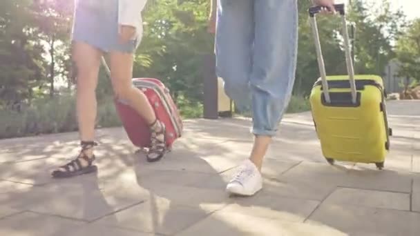 2人の幸せな若い観光客の女の子は近代的な都市景観の近くの都市でスーツケースと歩いています — ストック動画