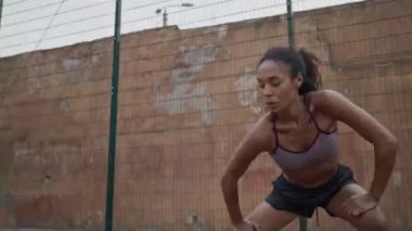 Spor giyimli sakin bir Afro-Amerikan kadın spor sahasında bacaklarını esnetiyor.