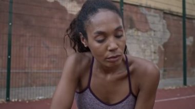 Spor kıyafetleri içinde yorgun bir Afrikalı Amerikalı kadın spor sahasında antrenman yaptıktan sonra alnından ter siliyor.
