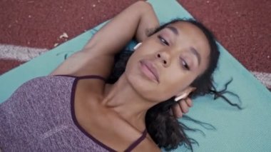 Spor kıyafetleri içinde sakin bir Afrikalı Amerikalı kadın spor sahasındaki yoga minderinde dinleniyor.