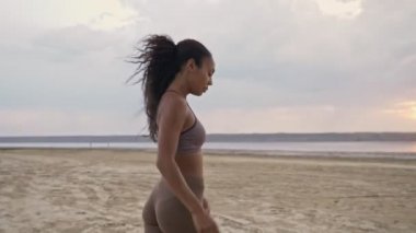 Sakin bir Afro-Amerikan kadın spor kıyafetleri içinde sabah antrenmanından önce sahilde yürüyor.