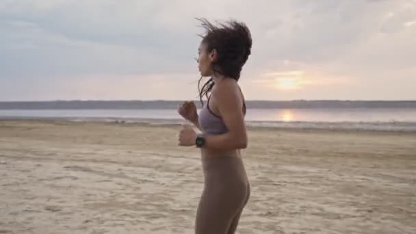 スポーツウェアを着たアフリカ系アメリカ人の女性が午前中にビーチで走っている — ストック動画