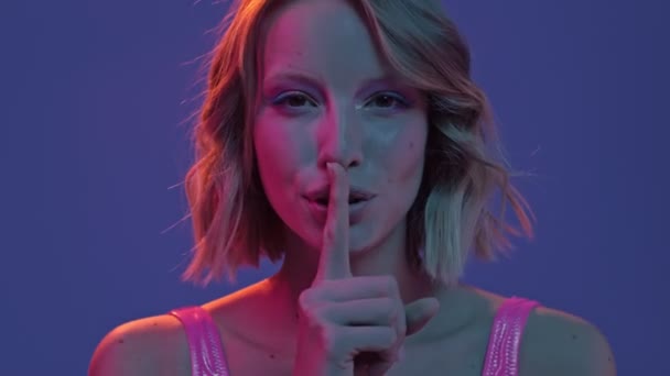 一个漂亮迷人的年轻女子的近照正在紫色霓虹灯的背景上做着一个沉默的手势 — 图库视频影像