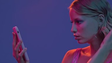 Moda makyajlı muhteşem genç bir kadının yakın plan görüntüsü telefonunda mor neon arka planda izole edilmiş selfie çekiyor.