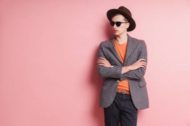 Ceket ve şapka giyen çekici bir gencin portresi pembe arka planda, şapkayla poz veriyor.