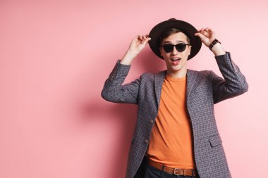 Çekici, ceketli ve şapkalı bir gencin portresi pembe arka planda izole bir şekilde duruyor, şapka takıyor.