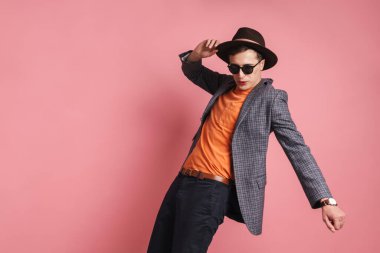 Ceket ve şapka giyen çekici bir gencin portresi pembe arka planda, şapkayla poz veriyor.