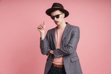 Ceket ve şapka giyen çekici bir gencin portresi pembe arka planda izole bir şekilde duruyor, şapka takıyor, sakız çiğniyor.