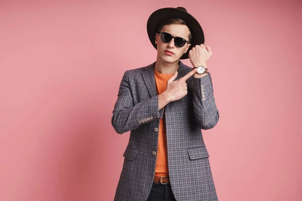 stock image Portrait of an attractive young man wearing jacket and hat standing isolated over pink background, checking time on his watch