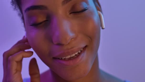 クローズアップ アフリカの女性が音楽を聴きながら 紫のネオンを背景に孤立した瞬間を楽しむイヤホン — ストック動画