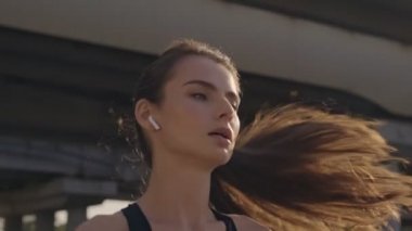 Kulaklıklı, yorgun ve genç bir kadın şehrin köprüsünün yakınında koşuyor.