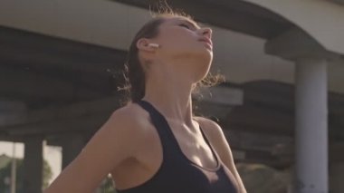 Sakin, güzel, kulaklıklı spor bir kadın, kentteki köprünün yakınındaki eğitimden sonra yan tarafa bakıyor.