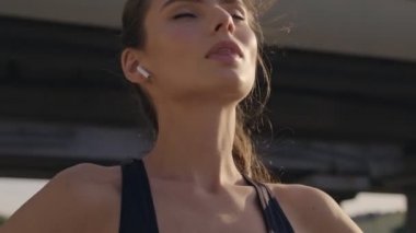 Kulaklıklı, güzel, sportif bir kadın şehir köprüsünün yakınında antrenman yapıyor.