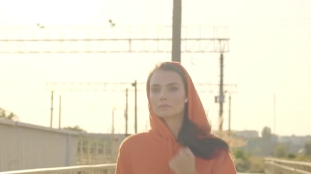 一个穿着橙色帽衫的强壮而又集中的年轻女子在桥上跑步 — 图库视频影像