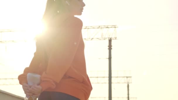 在阳光明媚的早晨 一位身穿橙色帽衫的瘦弱的年轻女子正在桥上伸展着腿 — 图库视频影像