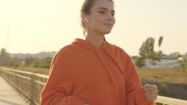 Spor giyim sektöründe mutlu genç bir kadın güneşli bir sabahta köprüde yürümekten keyif alıyor.
