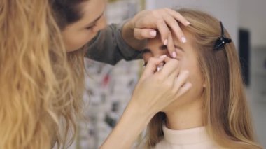 Odaklanmış profesyonel bir makyöz kuaförde siyah göz kalemiyle bir ok çiziyor.