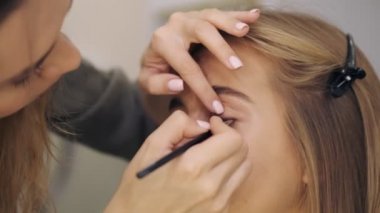 Sakin, profesyonel bir makyaj sanatçısının yakın çekim görüntüsü bir kuaförde genç ve güzel bir kadına doğal bir makyaj uyguluyor.