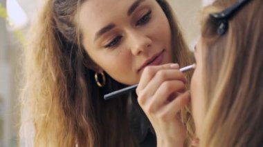 Profesyonel bir makyaj sanatçısının yakın plan görüntüsü kuafördeki genç sarışın kadına toz fırçası kullanarak doğal makyaj uyguluyor.