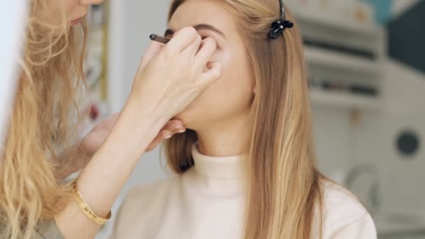 在一家美容院 一位年轻姑娘正坐在化妆师给她的眼睛涂天然眼影的时候 — 图库视频影像