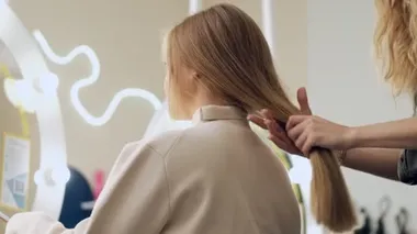 Profesyonel bir kuaförün alttaki görüntüsü müşterisinin uzun sarı saçlarına dokunuyor.