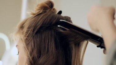 Profesyonel bir kuaförün yakın çekim görüntüsü güzellik salonundaki müşteriye ütü kullanarak bukleler yapmaktır.