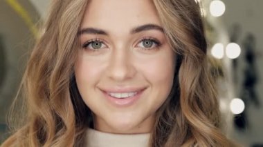 Güzel, gülümseyen, doğal makyajlı genç bir kız kameraya bakıyor.