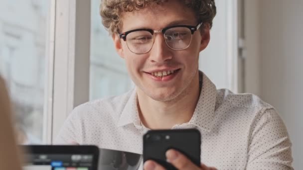 Joven Empresario Sonriente Con Gafas Está Usando Teléfono Móvil Mientras — Vídeos de Stock