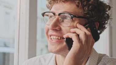 Gözlüklü çekici genç bir işadamının yakın plan görüntüsü, kafede iş arkadaşıyla otururken telefonla konuşuyor.