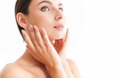 Güzel, genç, şehvetli, üstsüz kadın beyaz arka planda yalnız duruyor, poz veriyor, yüzlerine dokunuyor.