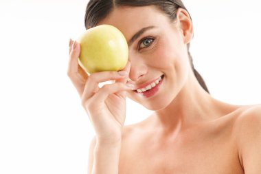 Çekici, gülümseyen, üstsüz, esmer bir kadının güzel portresi. Beyaz arka planda tek başına duruyor. Yeşil elma gösteriyor.