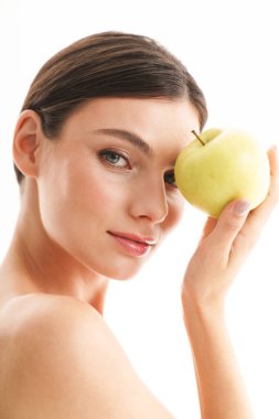 Çekici, üstsüz, esmer bir kadının güzel portresi. Beyaz arka planda izole bir şekilde duruyor. Yeşil elma gösteriyor.