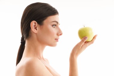 Çekici, üstsüz, esmer bir kadının güzel portresi. Beyaz arka planda izole bir şekilde duruyor. Yeşil elma gösteriyor.