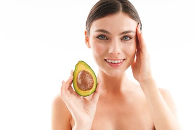 Çekici, gülümseyen, üstsüz, esmer bir kadının güzel portresi beyaz arka planda soyutlanmış, kesilmiş avokadoyu gösteriyor.
