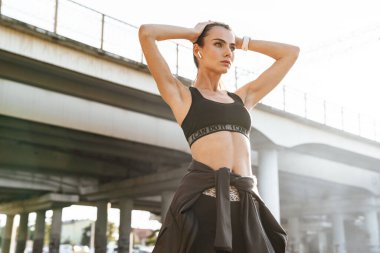 Dışarıda kulaklıkla müzik dinleyen genç ve güzel bir spor fitness kadınının görüntüsü..