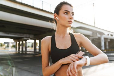 Güzel bir spor fitness kadınının fotoğrafı. Dışarıda kulaklıkla saat kullanarak müzik dinliyor..
