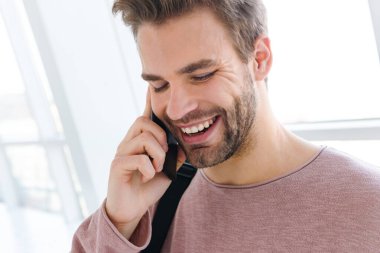 Çantalı genç sakallı bir adamın parlak pencerenin önünde akıllı bir telefonla konuşurken görüntüsü.