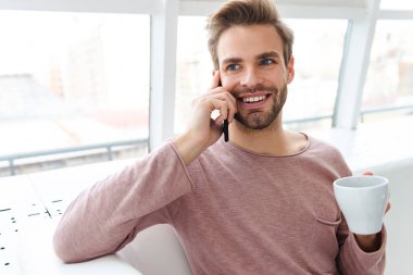 Kafede pencerenin kenarında otururken akıllı telefondan konuşan sakallı bir genç resmi.