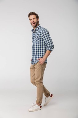 Ekose gömlek giyen, elleri ceplerinde beyaz arka planda poz veren gülen genç adamın portresi.